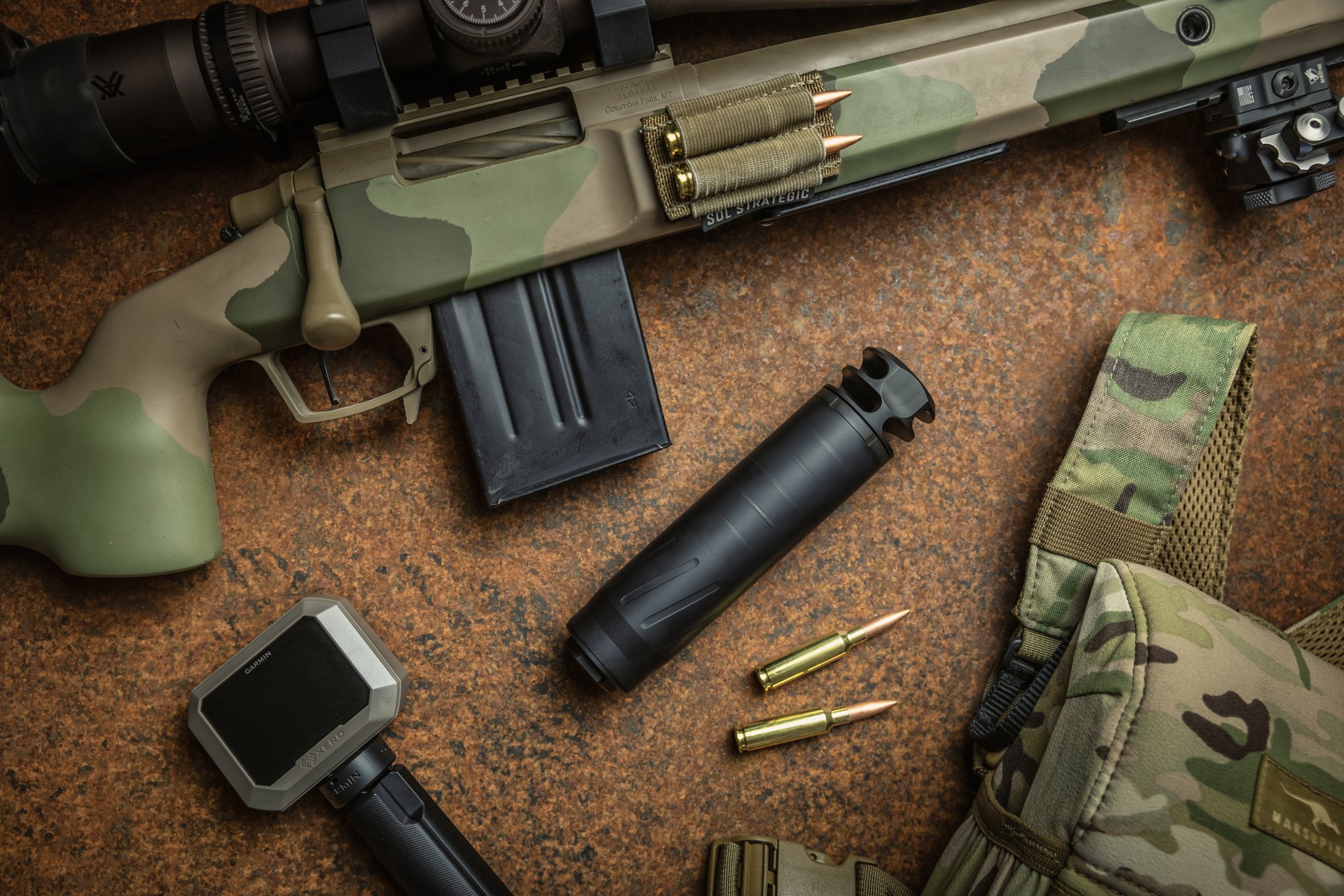 BANISH COMP 6.5 suppressor with two-port brake installed, beside a camo precision bolt-action rifle and 6.5mm cartridges